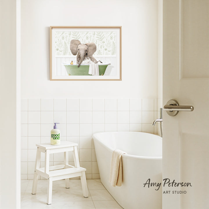 A framed image of an elephant in a bathtub is hanging on a white tiled wall above a white bathtub in a bathroom.