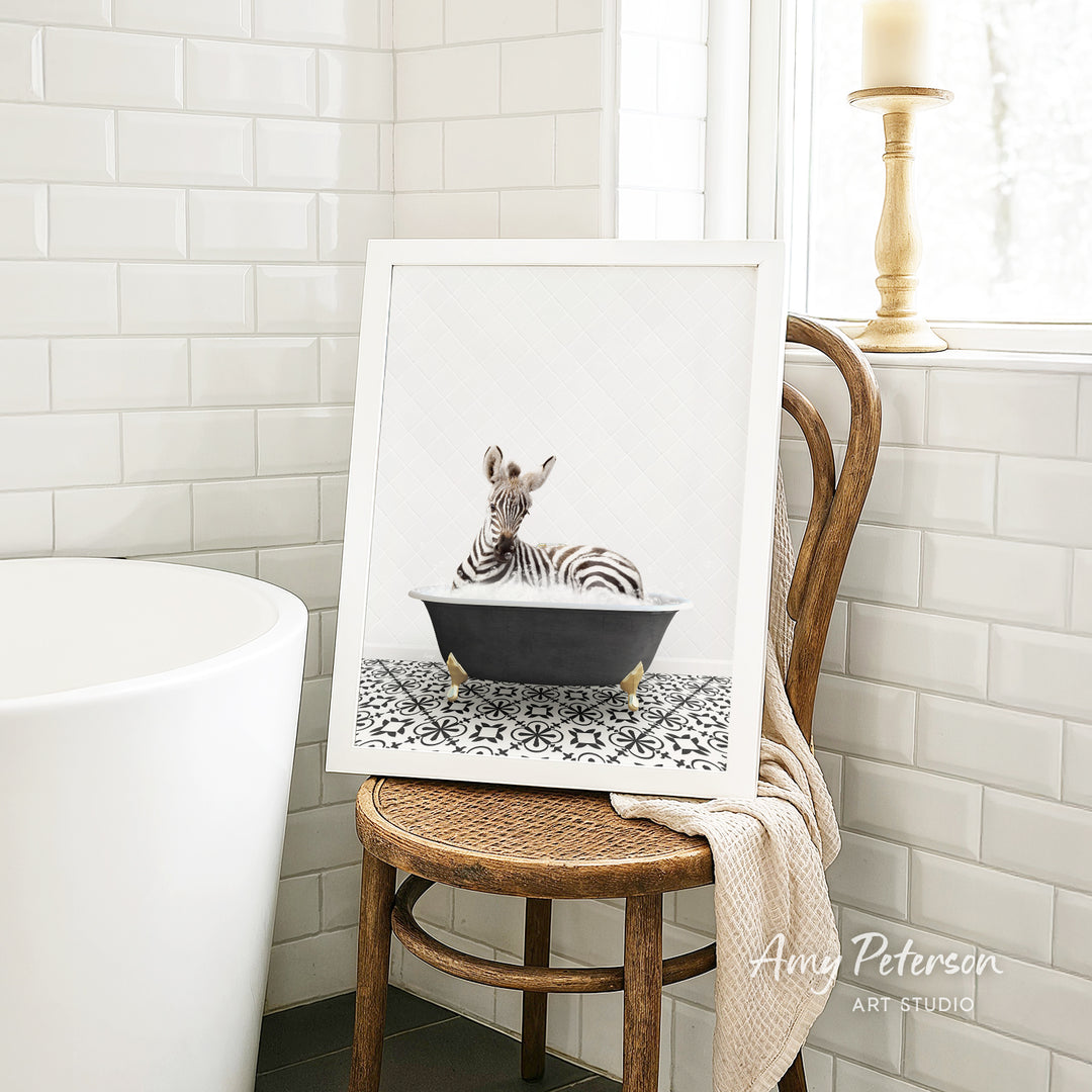 A framed image of a zebra sitting in a bathtub is displayed on a wooden chair in a bathroom setting.