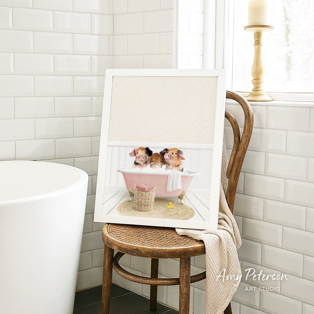 A framed image of two adorable puppies sitting in a pink bathtub, surrounded by a basket of bath toys, is displayed on a wooden chair in a bathroom setting.