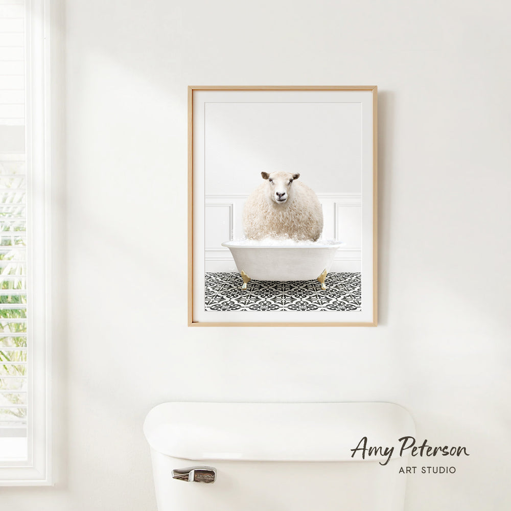 A framed image of a sheep sitting in a bathtub is hanging on a white wall in a bathroom.