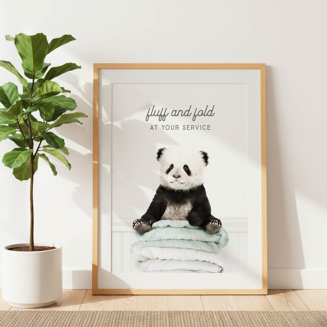 A framed image of a panda bear sitting on a stack of towels, with the text "fluff and fold at your service" written above the image.