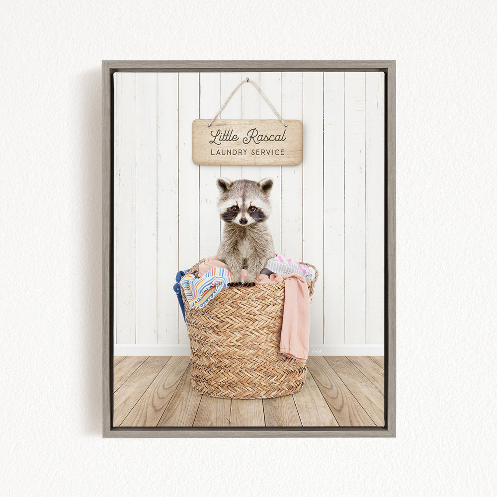 A raccoon sitting in a woven laundry basket, with a sign above that reads "Little Racal Laundry Service".
