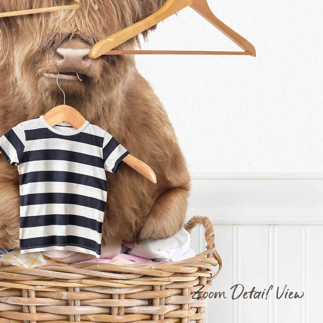 A large, furry animal, possibly a yak or a similar creature, is sitting inside a wicker basket filled with clothing items, including a striped shirt.