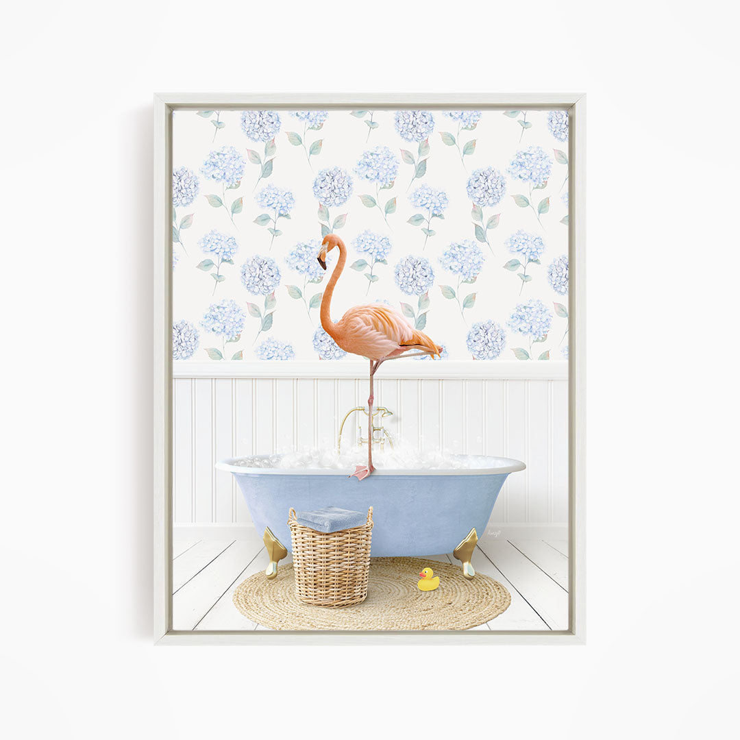 A pink flamingo stands on the edge of a blue bathtub, surrounded by a wicker basket, a yellow rubber duck, and a floral patterned wall behind it.