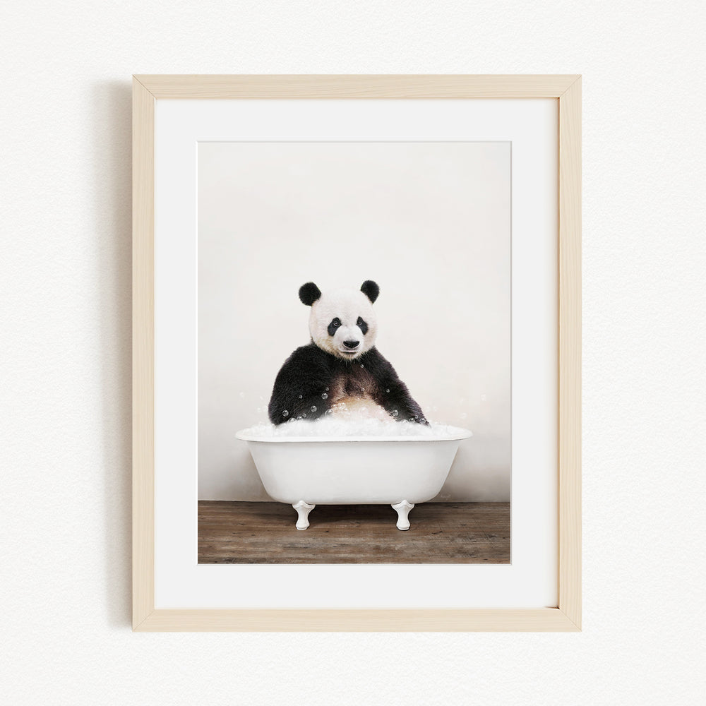 A panda bear sitting in a white bathtub filled with bubbles, looking directly at the camera.
