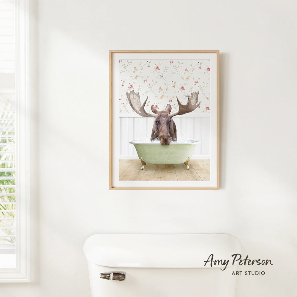 A framed image of a moose sitting in a bathtub, with a floral pattern on the wall behind it.