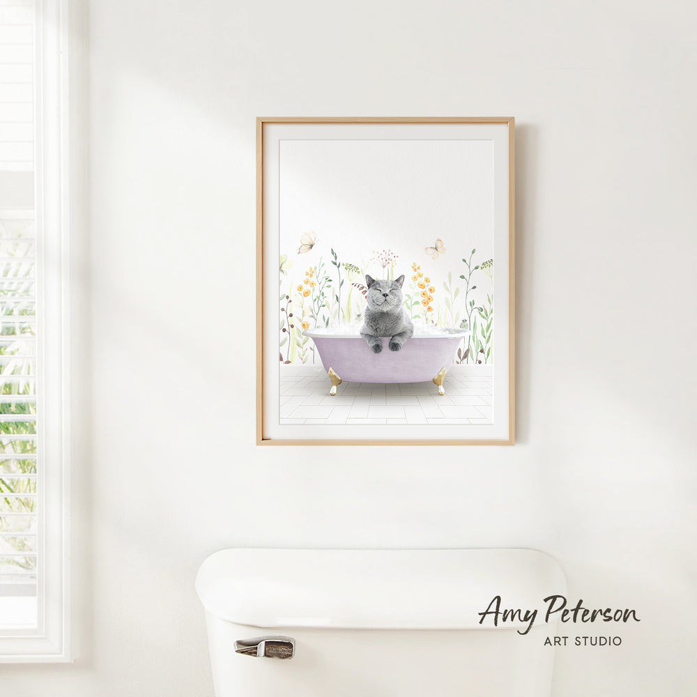 A framed illustration of a cat sitting in a bathtub, surrounded by flowers and butterflies, is hanging on a white wall.