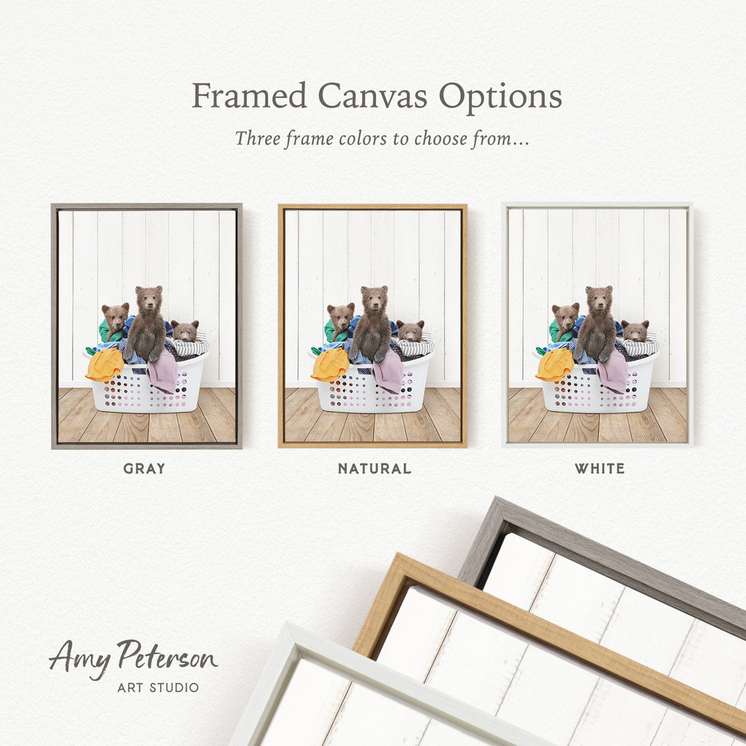 three framed canvas options, each featuring a brown bear sitting in a basket filled with laundry. The options include a gray frame, a natural frame, and a white frame.