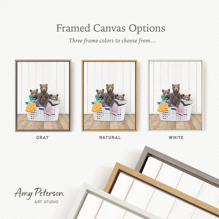 three framed canvas options, each featuring a brown bear sitting in a basket filled with laundry. The options include a gray frame, a natural frame, and a white frame.
