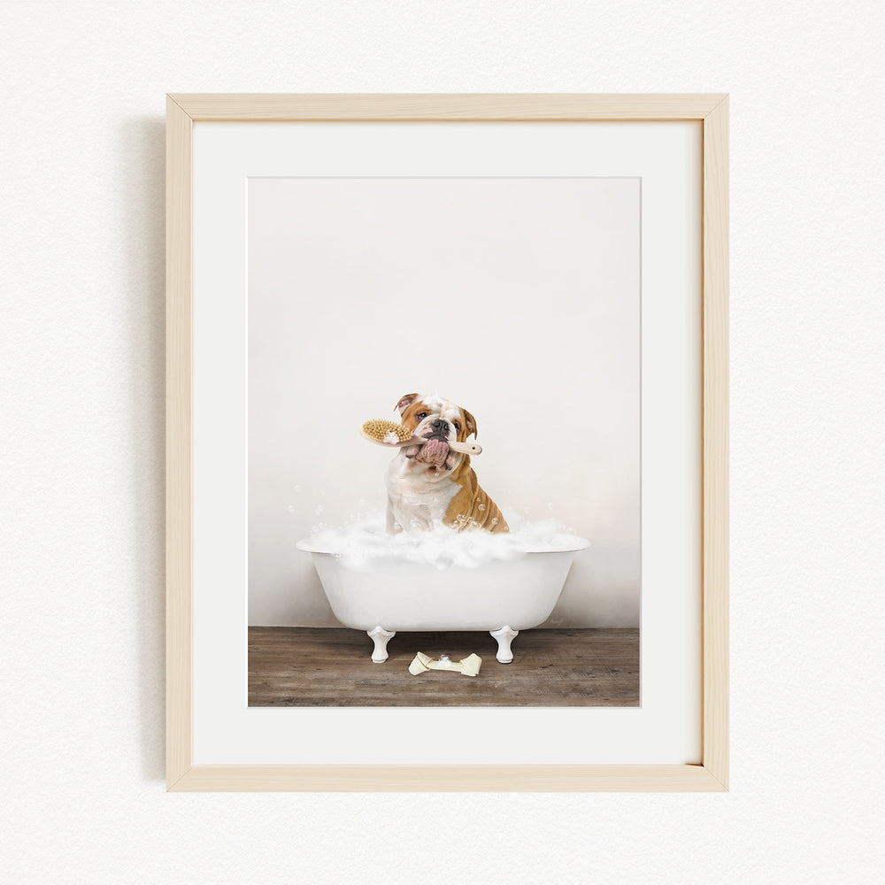 A dog sitting in a white bathtub filled with bubbles, with a bone on the floor.