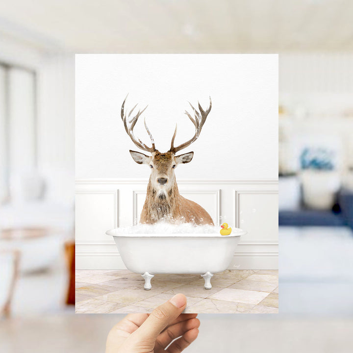 A deer with antlers is sitting in a bathtub filled with bubbles, with a yellow rubber duck floating in the water.
