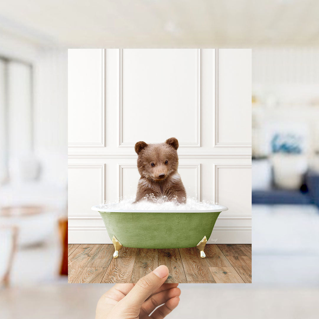 A small brown bear sitting in a green bathtub filled with bubbles, with a blurred background suggesting a bathroom setting.