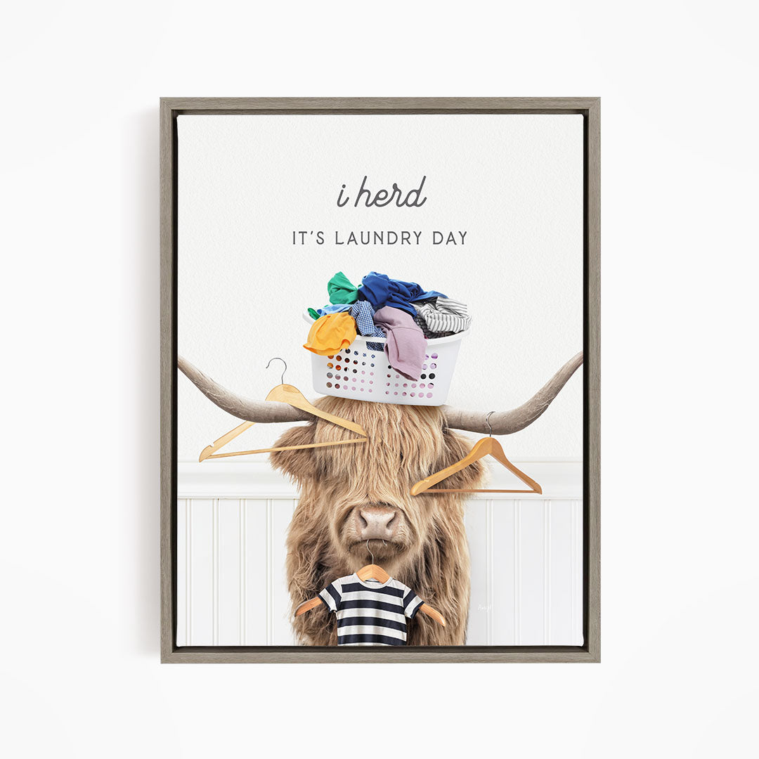 A framed image depicting a cow with a basket of laundry on its head, accompanied by the text "It's Laundry Day" and a humorous caption.