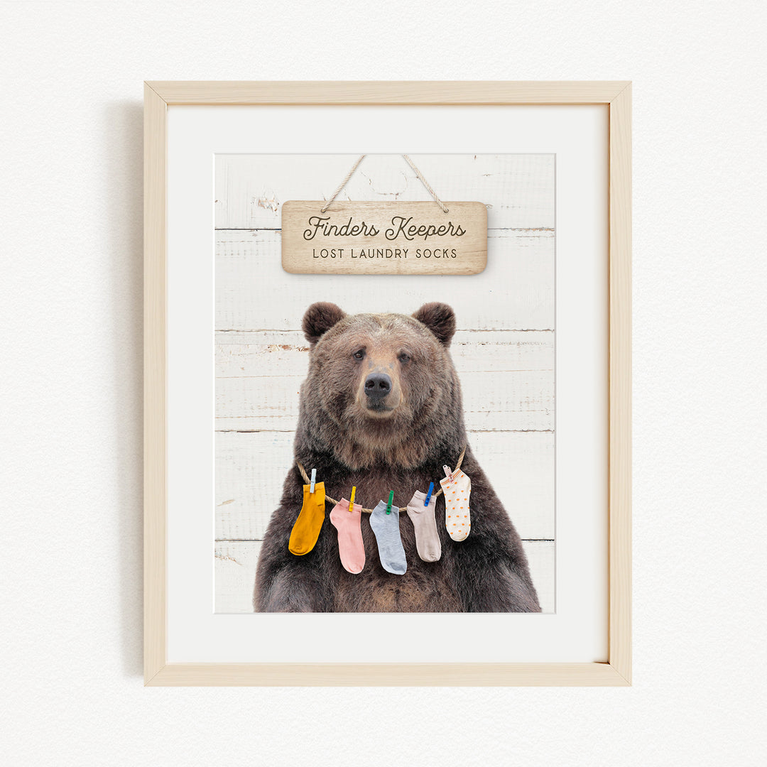 A framed image of a brown bear wearing colorful socks hanging on a clothesline.