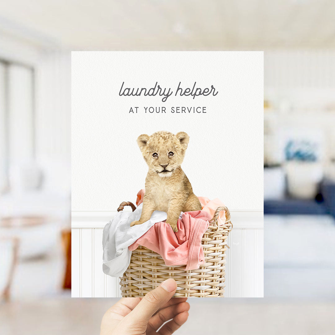 A hand holding a card with a picture of a young lion cub sitting in a wicker basket filled with clothes.