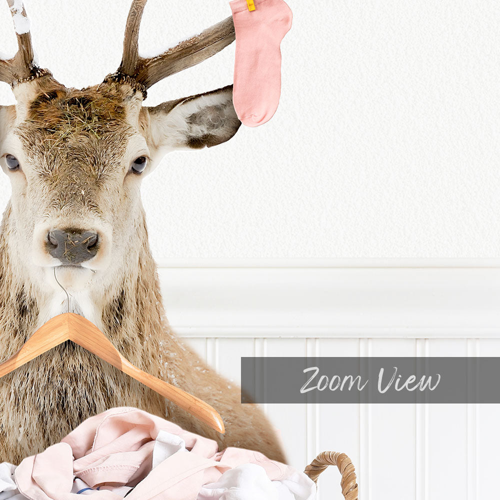 A deer with antlers is sitting on a clothesline, holding a pink sock in its mouth.