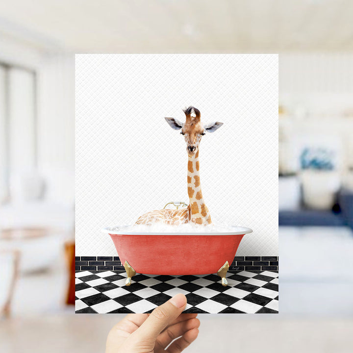 A giraffe sitting in a red bathtub filled with bubbles, with a hand holding the image up to the camera.