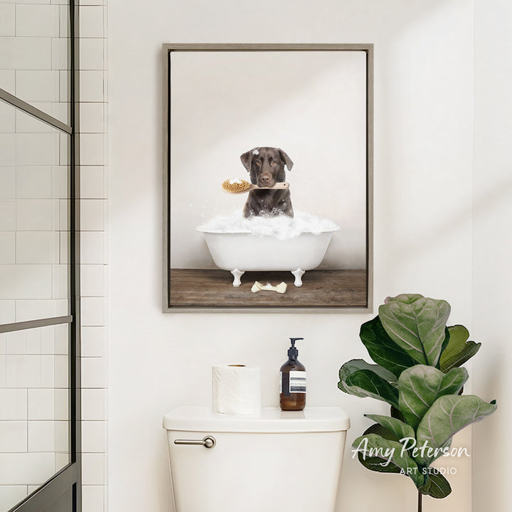 A framed image of a dog sitting in a bathtub, surrounded by bubbles, is displayed on the wall above a white toilet in a bathroom.
