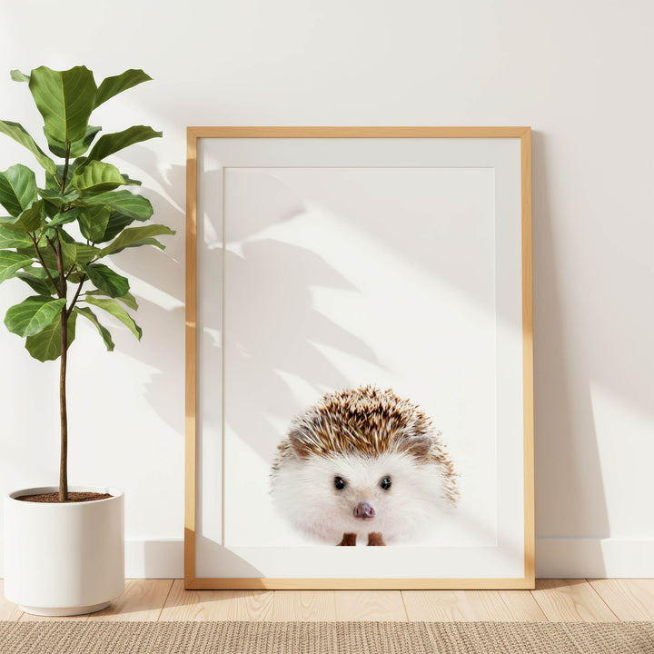 a framed picture of a hedgehog, placed on a wooden floor next to a potted plant.