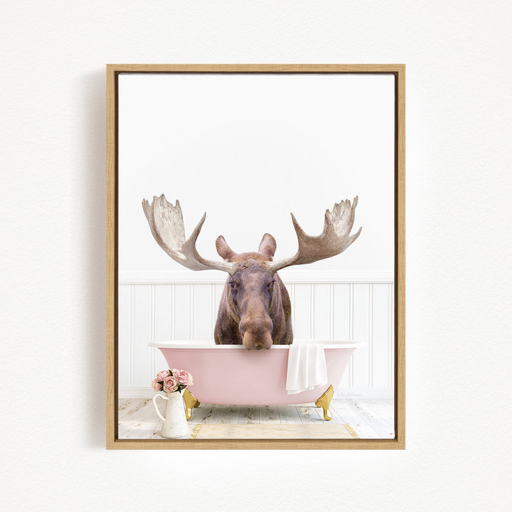 A moose with large antlers is sitting in a pink bathtub, surrounded by pink flowers and a white vase.