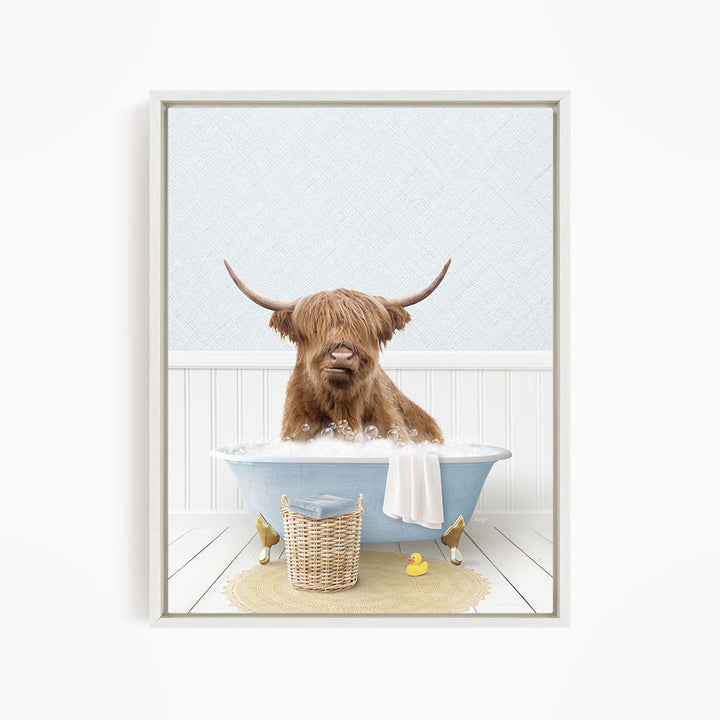 A brown cow with long horns is sitting in a blue bathtub filled with water, surrounded by a yellow rubber duck and a basket.