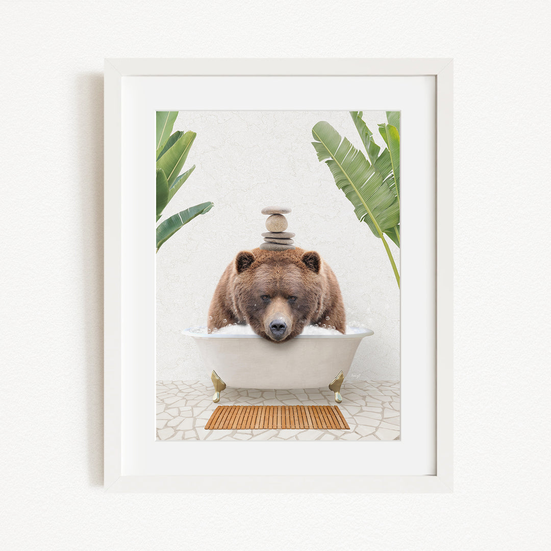 A brown bear is sitting in a white bathtub filled with water, surrounded by green plants and a wooden mat on the floor.