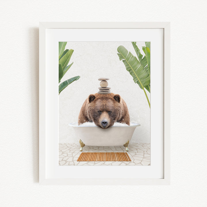 A brown bear is sitting in a white bathtub filled with water, surrounded by green plants and a wooden mat on the floor.