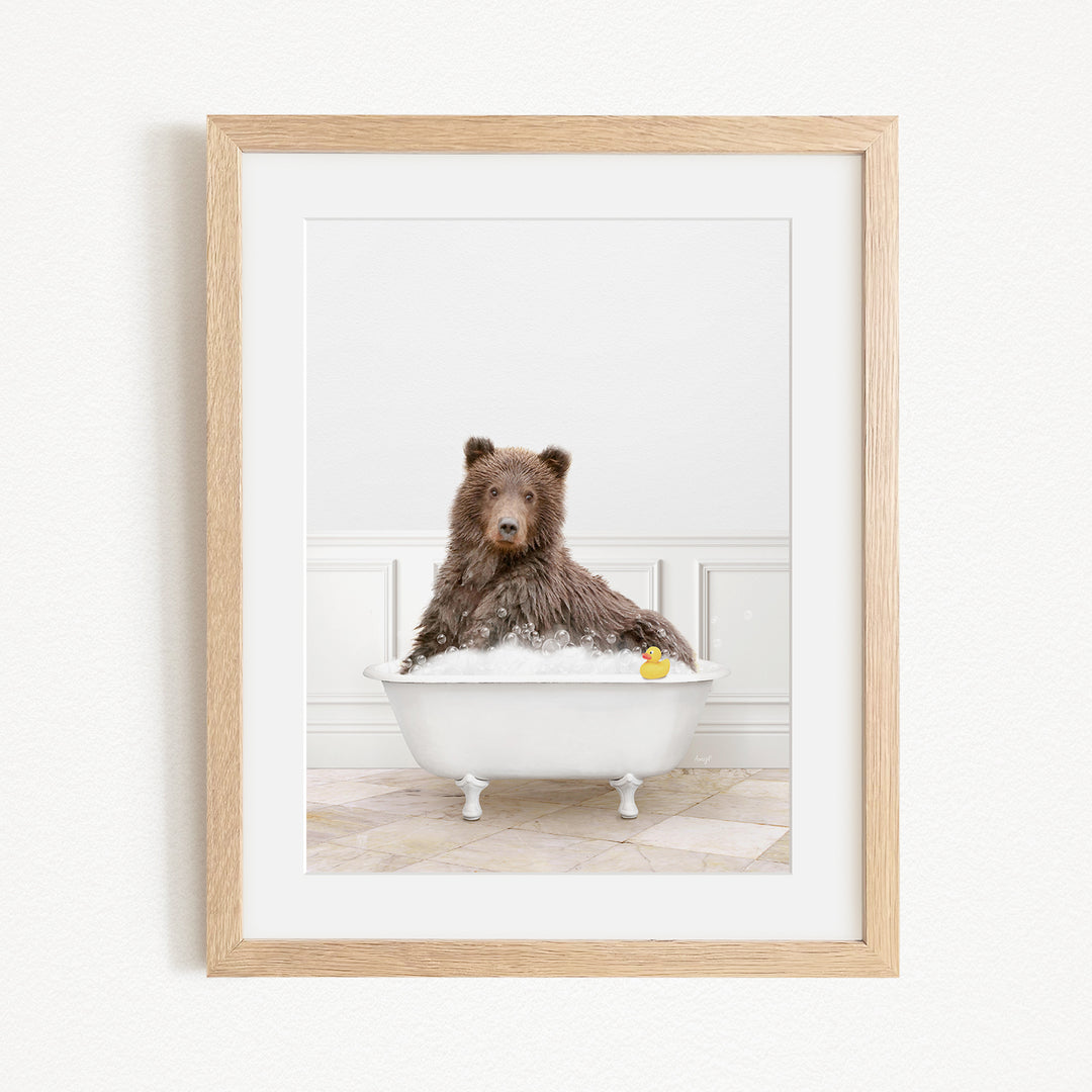A brown bear sitting in a white bathtub filled with bubbles, with a yellow rubber duck floating in the water.