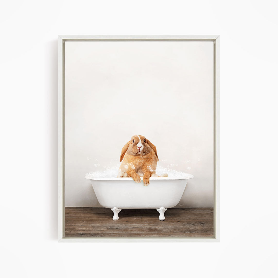 A brown rabbit sitting in a white bathtub filled with water, with bubbles around it.
