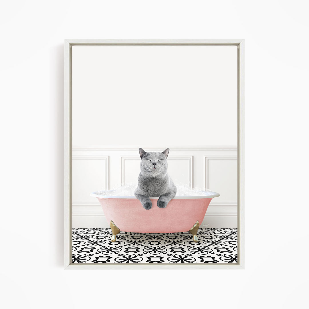 A gray cat sitting in a pink bathtub filled with bubbles, surrounded by a black and white patterned floor.