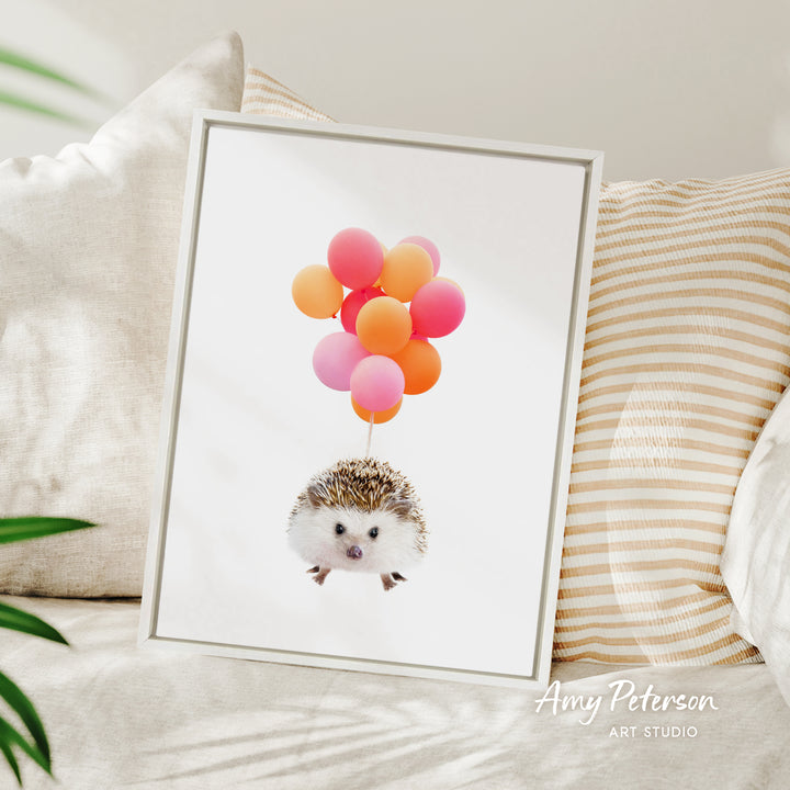 A framed image of a hedgehog with colorful balloons floating above it, placed on a bed with striped pillows.