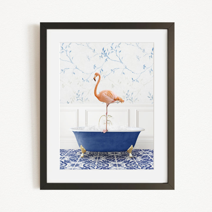 A framed image depicting a pink flamingo standing on the edge of a blue bathtub filled with water, set against a floral wallpaper background.