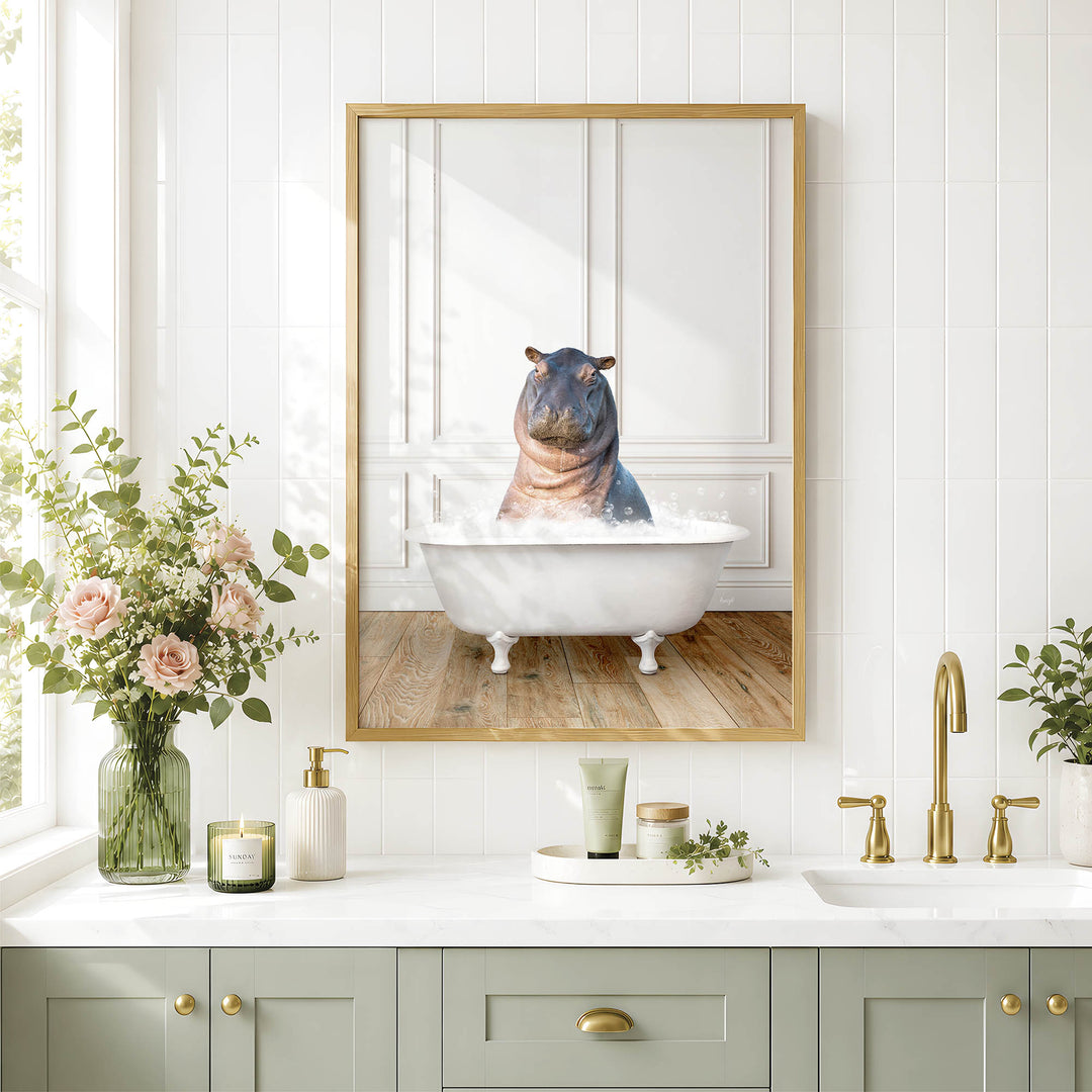 A framed image of a hippopotamus sitting in a bathtub is displayed on a white tiled wall above a bathroom vanity with a sink, green cabinets, and a vase of flowers.