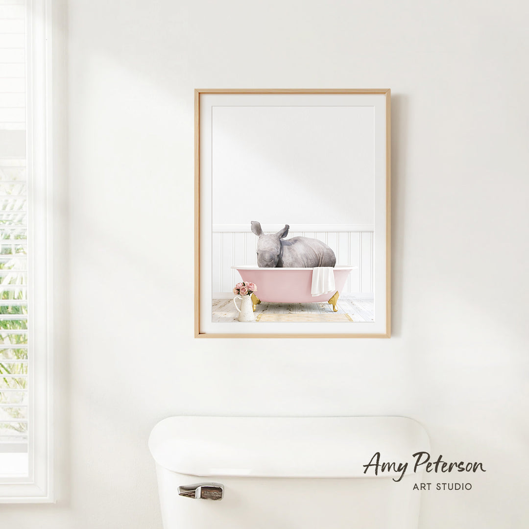 A framed image of a gray rabbit sitting in a pink bathtub, with a white toilet and a window in the background.