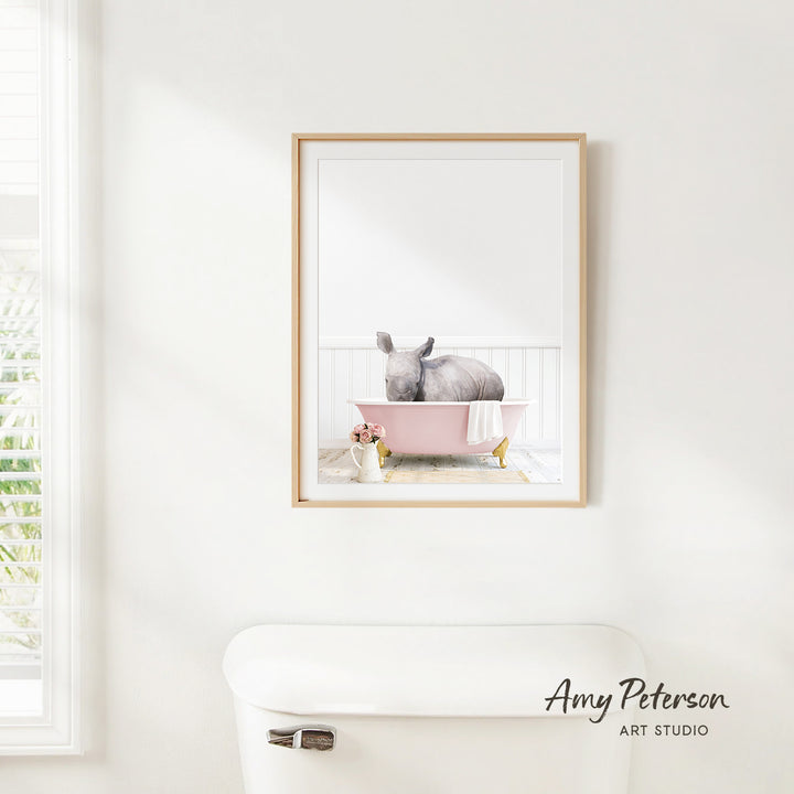 A framed image of a gray rabbit sitting in a pink bathtub, with a white toilet and a window in the background.