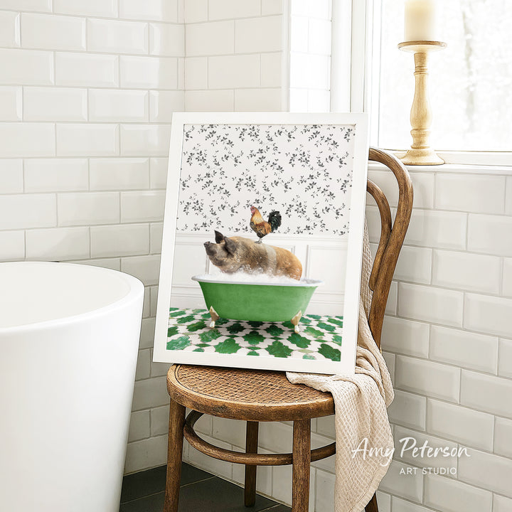 A framed image of a cat sitting in a green bathtub, with a rooster perched on the edge of the tub, is displayed on a wooden chair in a bathroom setting.