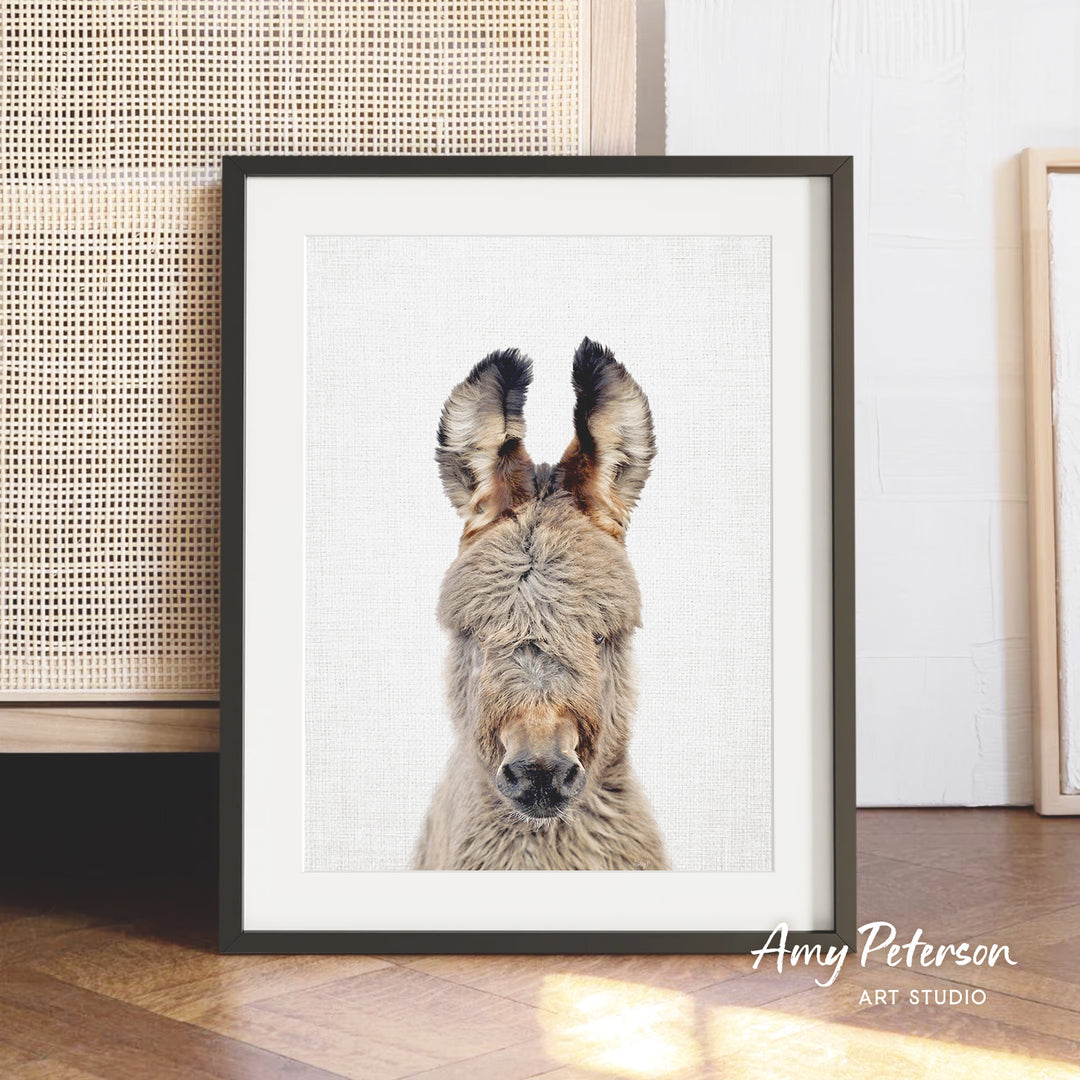 A framed photograph of a donkey's head is displayed on a wooden floor, with a beige woven basket visible in the background.