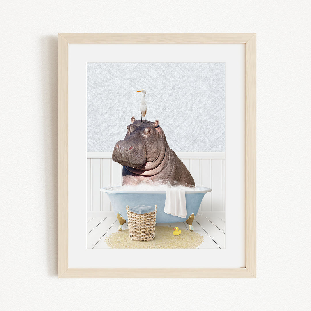 A framed image depicting a hippopotamus sitting in a bathtub, with a bird perched on its head.
