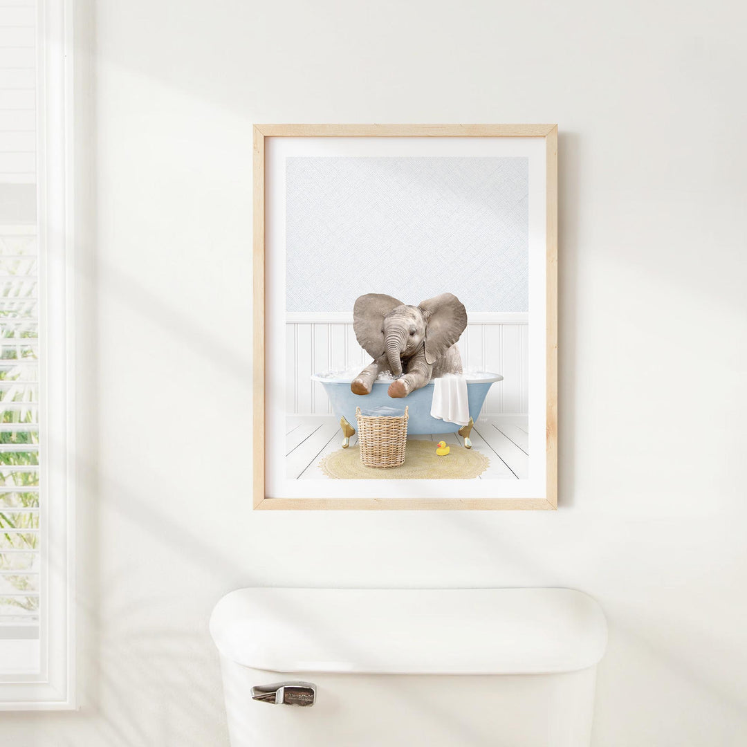 A framed image of a baby elephant sitting in a bathtub, surrounded by various objects such as a basket and a towel.