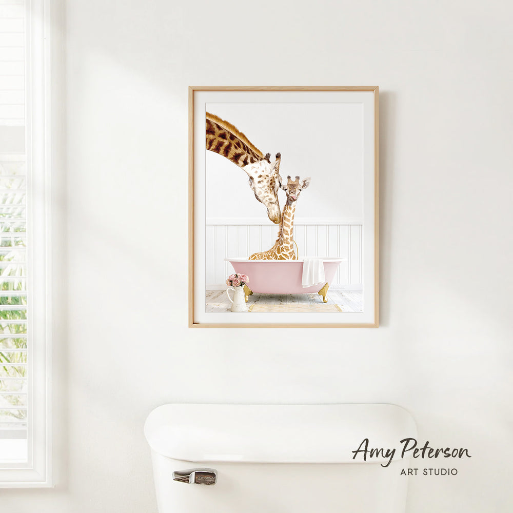 A framed image of two giraffes sitting in a pink bathtub, with one giraffe appearing to be giving the other a bath.