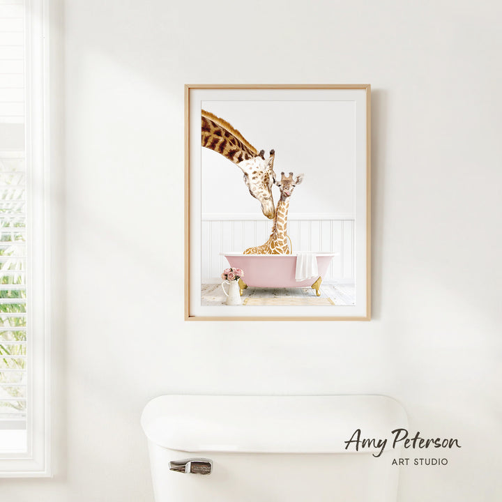 A framed image of two giraffes sitting in a pink bathtub, with one giraffe appearing to be giving the other a bath.