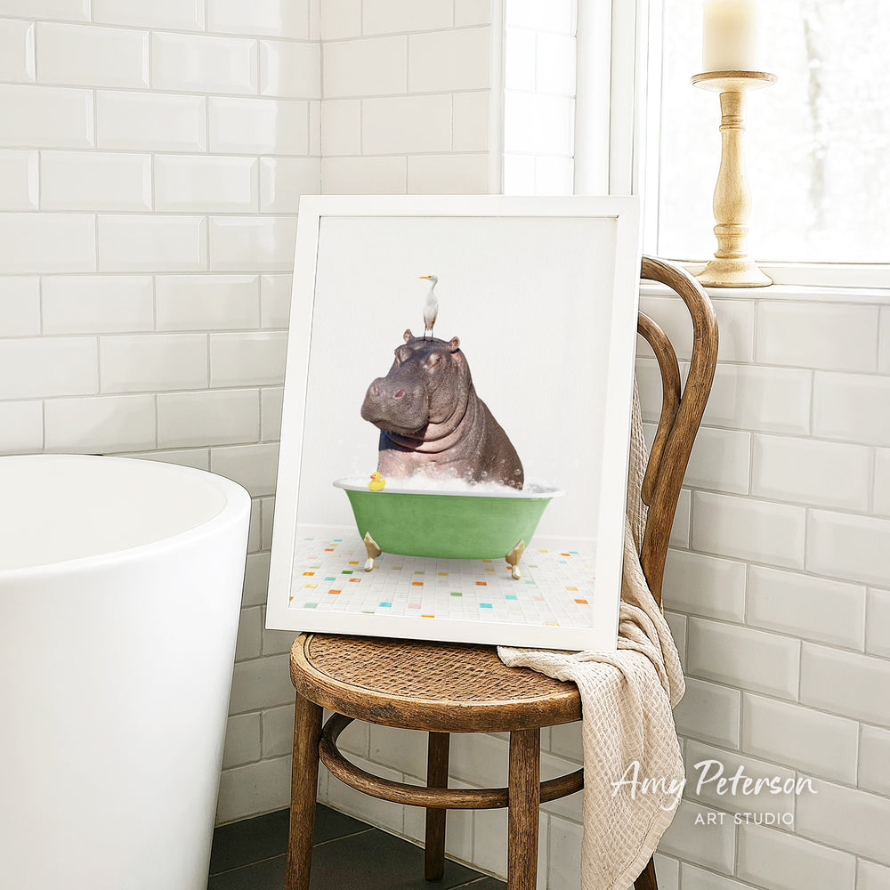 A framed image of a hippopotamus sitting in a green bathtub, surrounded by colorful tiles, is displayed on a wooden chair in a bathroom setting.