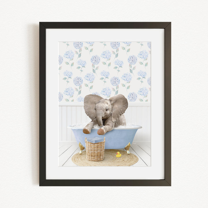 A baby elephant sitting in a blue bathtub, surrounded by a floral patterned wall and a basket of rubber ducks.