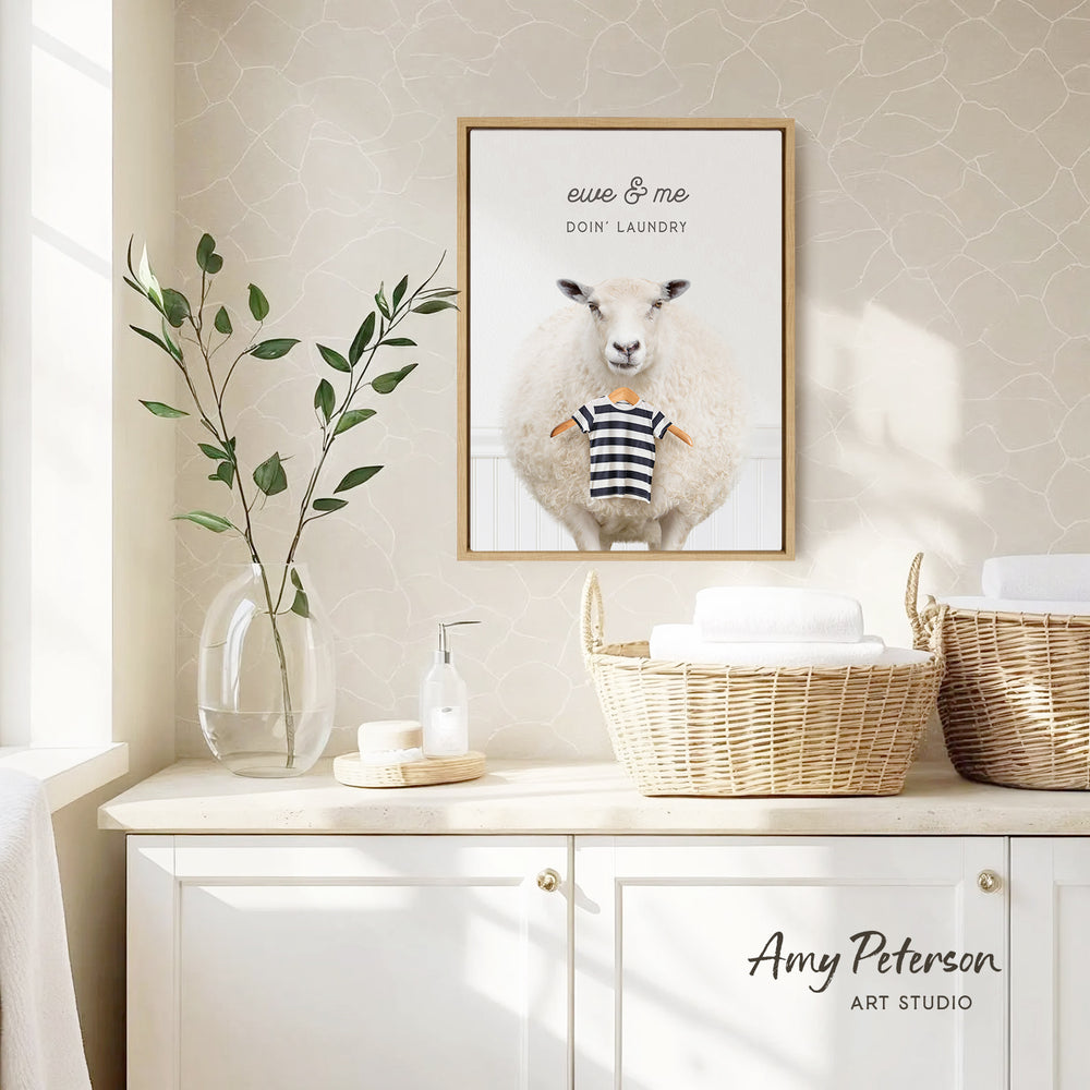 a framed picture of a sheep wearing a striped shirt, hanging on a wall above a white cabinet with baskets below it.