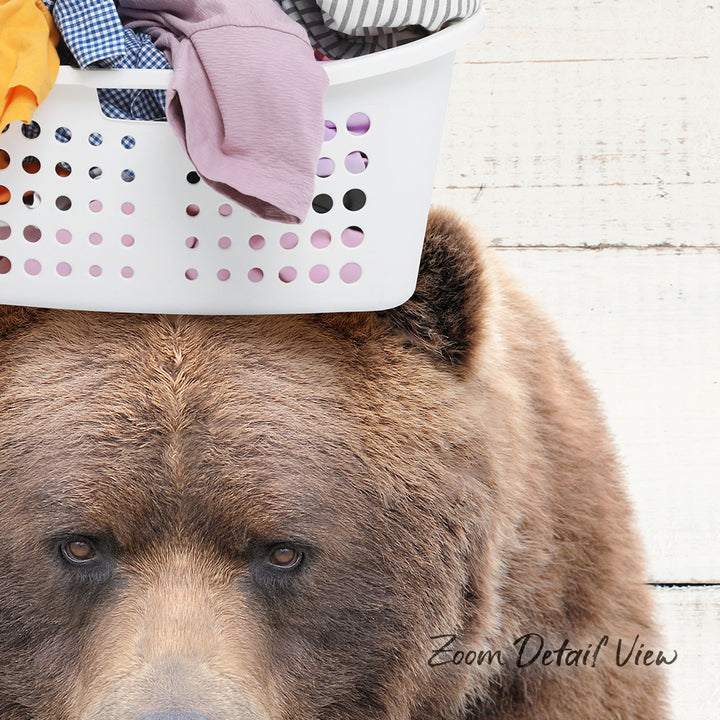 A close-up of a brown bear's face peering over a laundry basket filled with clothes.