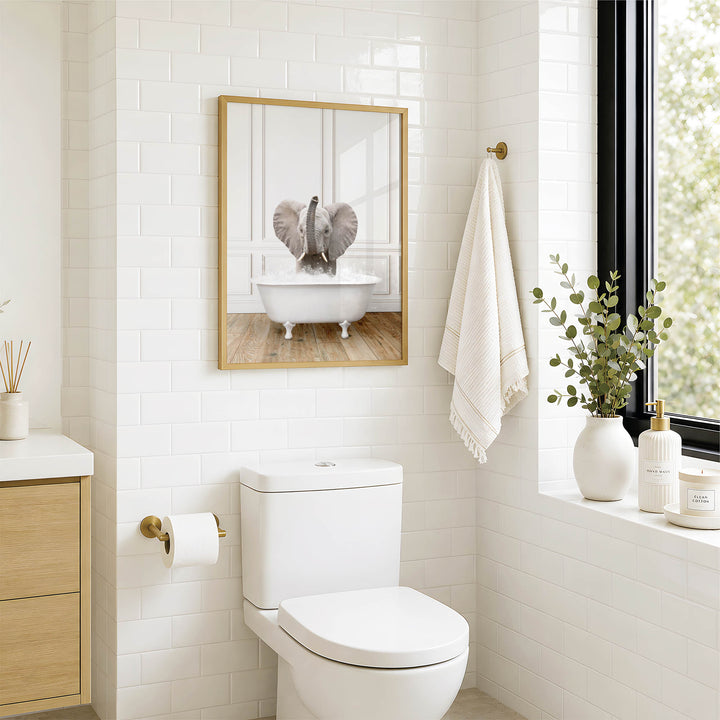 a bathroom with a white toilet, a framed picture of an elephant in a bathtub, and a towel hanging on a rack.