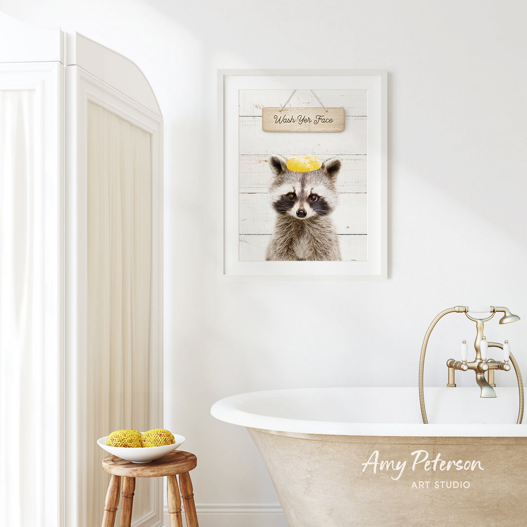 a bathroom with a framed picture of a raccoon wearing a yellow hat, a wooden stool with a bowl of fruit, and a clawfoot bathtub.