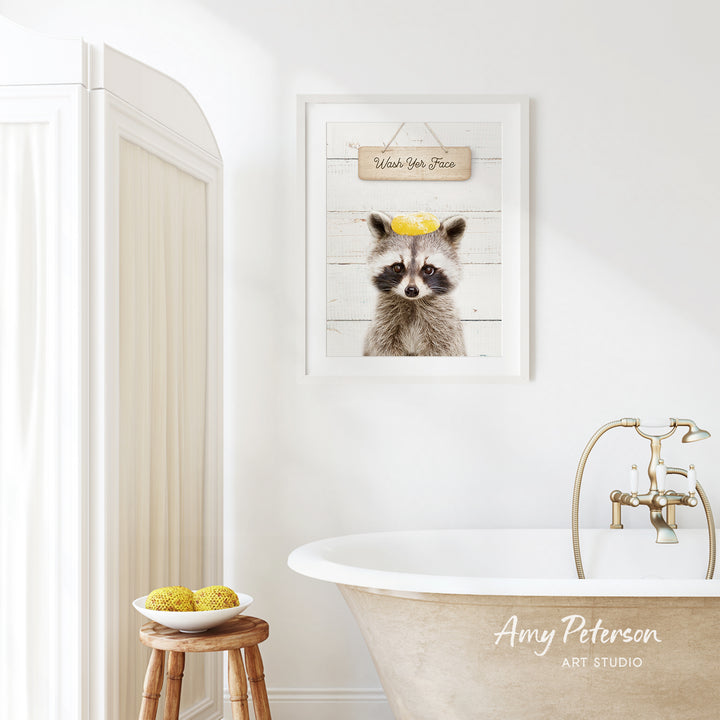 a bathroom with a framed picture of a raccoon wearing a yellow hat, a wooden stool with a bowl of fruit, and a clawfoot bathtub.