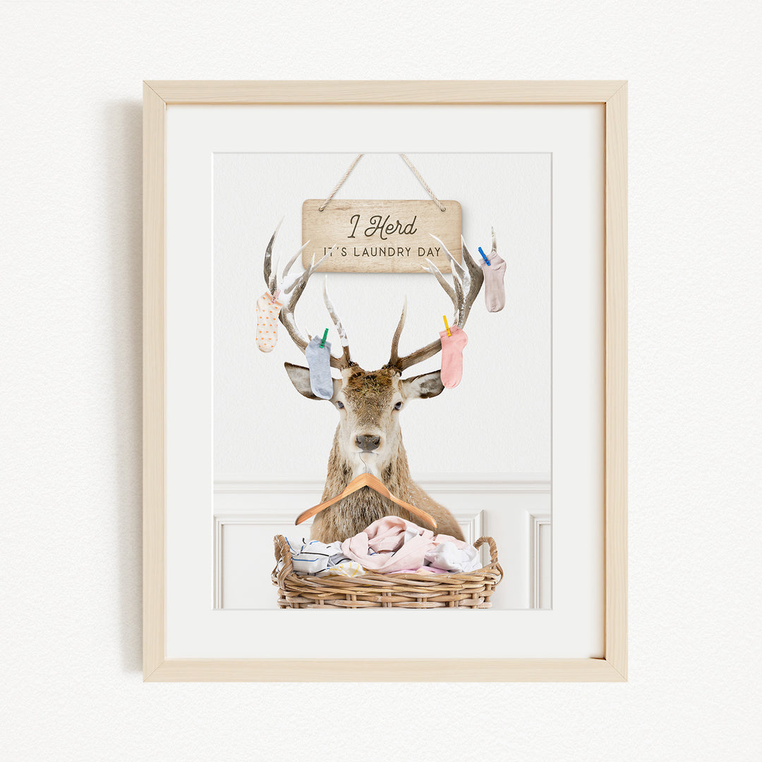 A framed image depicting a deer with antlers hanging from its head, holding a basket filled with clothes, and a sign above it that says "I hold it's laundry day".
