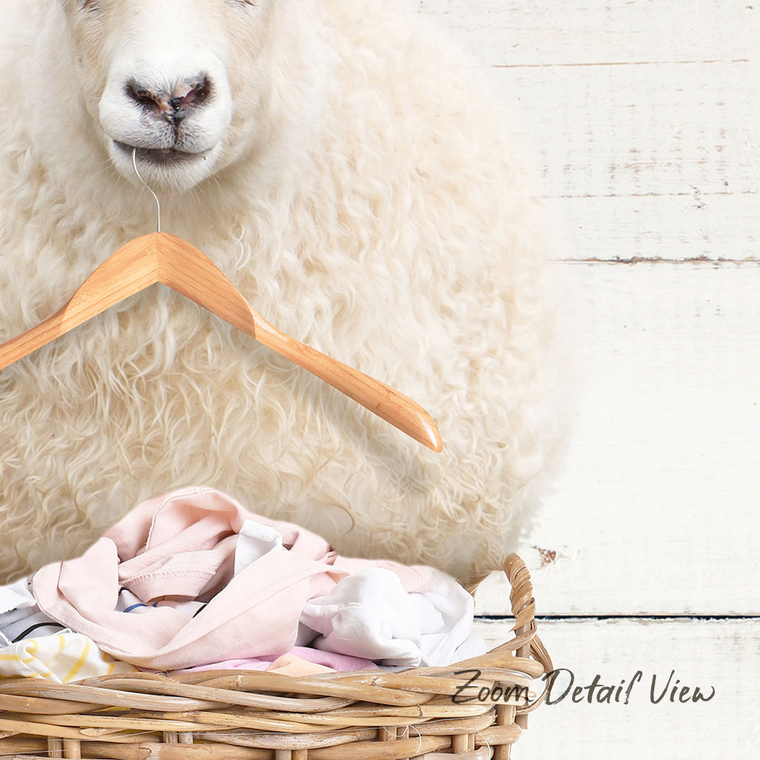 A fluffy white sheep is standing next to a wicker basket filled with clothes, with a wooden hanger attached to the basket.